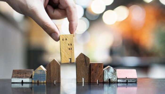 Hand,Choosing,Mini,Wood,House,Model,From,Model,And,Row